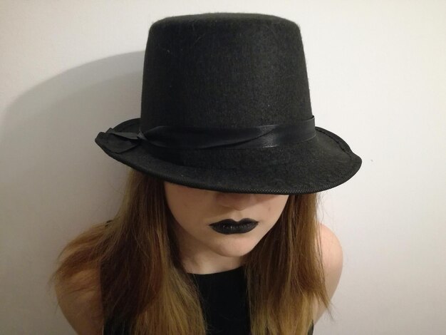 High angle view of woman wearing black hat and lipstick while standing against white wall