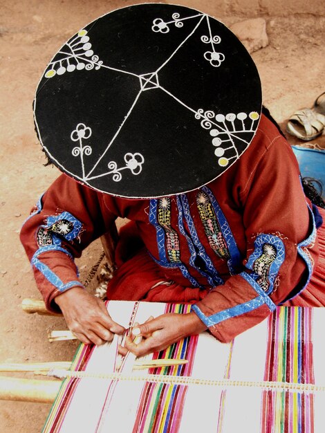 Photo high angle view of woman wearing hat while weaving textile outdoors