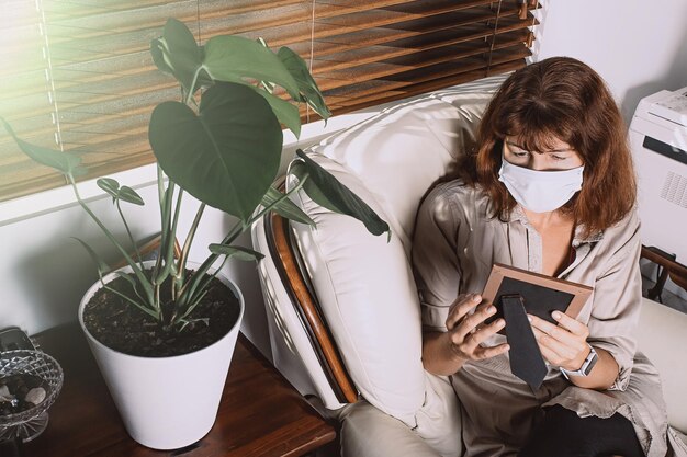 Photo high angle view of woman wearing mask looking picture while sitting at home