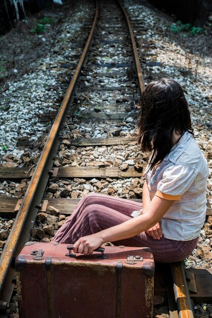 鉄道線路に座っているスーツケースを持った女性の高角度の視点