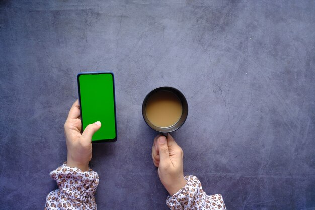 Vista dall'alto della mano delle donne che usa lo smartphone e beve caffè