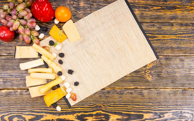 コピースペースのある素朴な木製のテーブルにさまざまなチーズと新鮮な果物と木の板の高角度ビュー