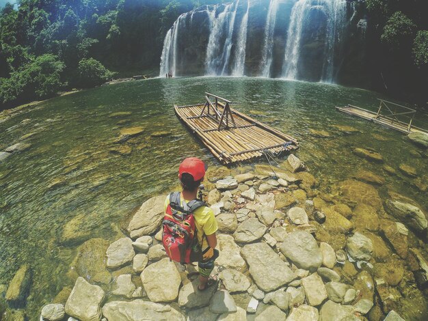 Foto vista ad alto angolo di un giovane con uno zaino in piedi sulla riva del fiume