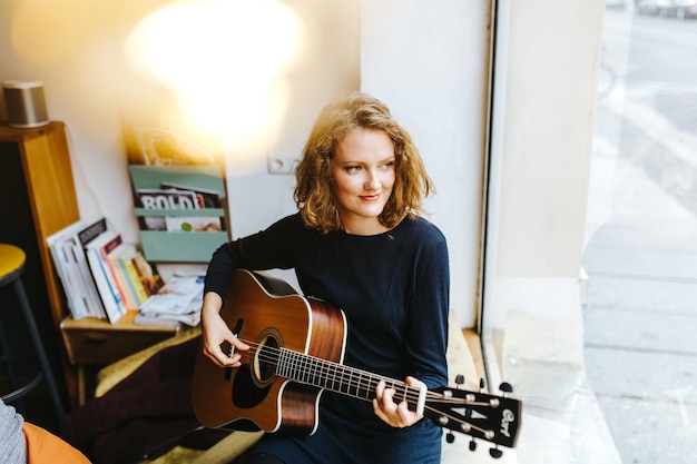 High angle view of young woman playing guitar by window at home