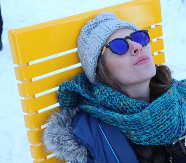 High angle view of young woman in warm clothing resting on chair during winter