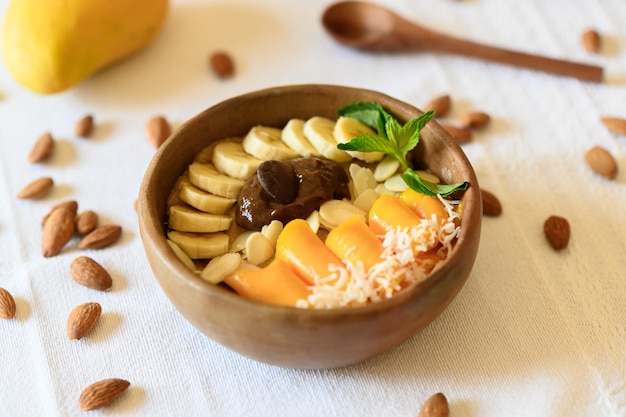 High angle of wooden bowl filled with fresh banana and mango slices almonds and melted chocolate