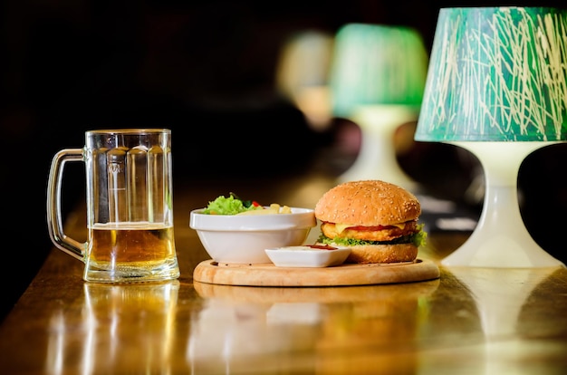 High calorie snack hamburger and french fries and tomato sauce\
on wooden board delicious burger burger with cheese meat and salad\
pub food and mug of beer fast food concept burger menu