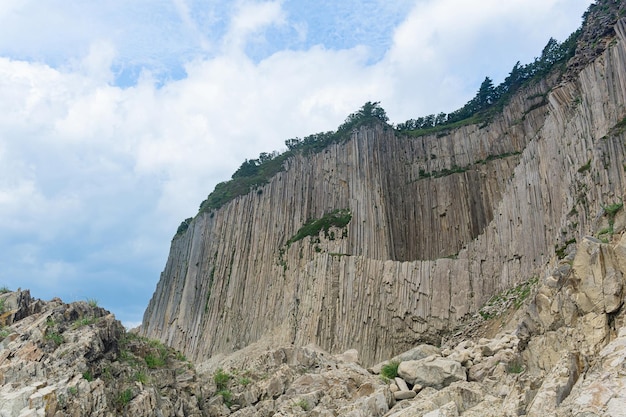 высокая прибрежная скала, образованная застывшими лавовыми каменными колоннами, мыс Столбчатый на острове Кунашир