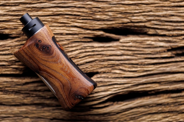 High end rebuildable dripping atomizer with natural stabilized walnut wood regulated box mods on rustic natural wood texture background vaporizer equipment