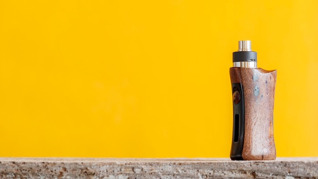 High end rebuildable dripping atomizer with stabilized natural walnut wood regulated box mods in yellow texture background with copy space vaping device selective focus