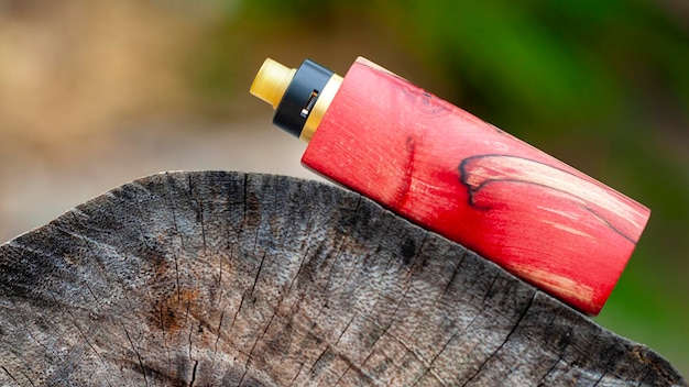 Photo high end red natural stabilized wood regulated box mods with rebuildable dripping atomizer on natural timber wood texture background vaporizer equipment selective focus