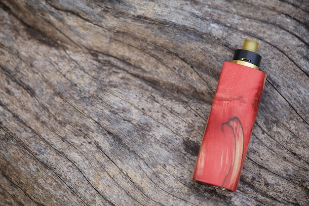 High end red natural stabilized wood regulated box mods with rebuildable dripping atomizer on natural timber wood texture background, vaporizer equipment, selective focus