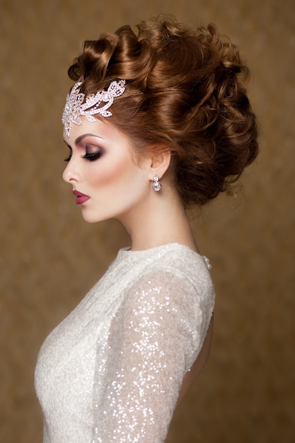 High fashion hairstyle of a red haired woman, with bridal make-up and accessories, wearing bridal dress