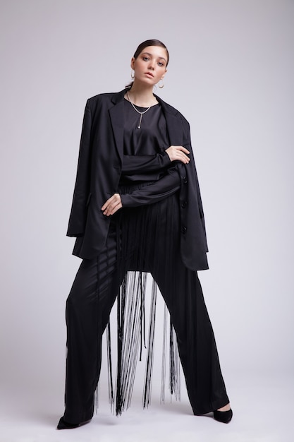 High fashion photo of woman in black jacket blouse fringe pants accessories on gray background