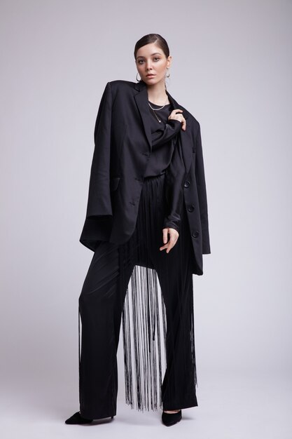 High fashion photo of woman in black jacket blouse fringe pants accessories on gray background