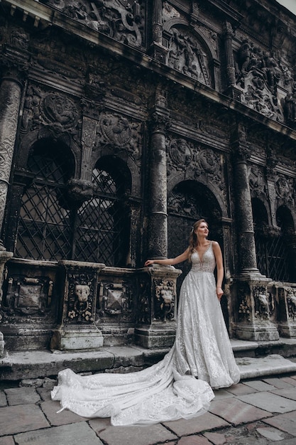 High fashion portrait of young elegant woman outdoor Bride in white dress near old building