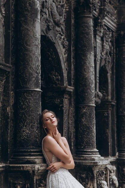 High fashion portret van jonge elegante vrouw buiten bruid in witte jurk in de buurt van oud gebouw