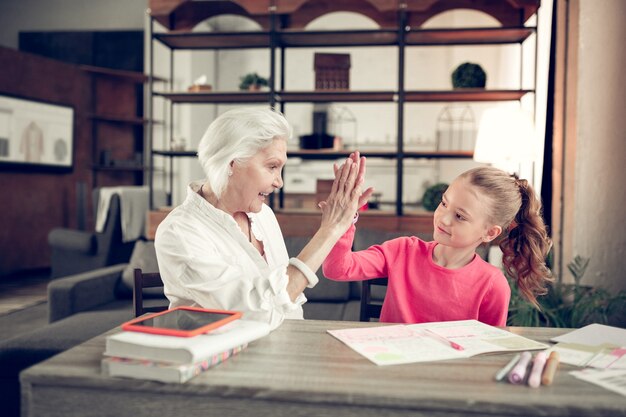 High five geven. liefdevolle kleindochter geeft high five aan haar coole grootmoeder na huiswerk te hebben gemaakt