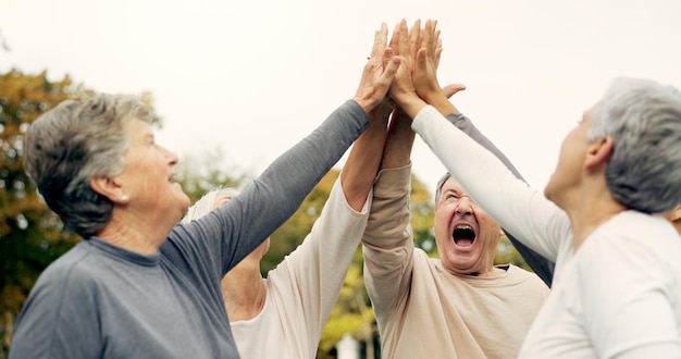 High five-ondersteuning en een groep oudere vrienden samen in een park voor motivatie succes of viering Teambouw partnerschap en gemeenschap met oudere mensen banden buiten in een tuin