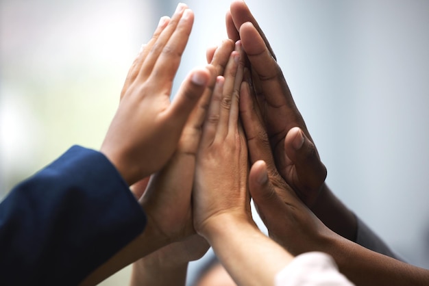 Photo high five for teamwork shot of a group of unrecognizable businesspeople holding up their hands for a high five in an office