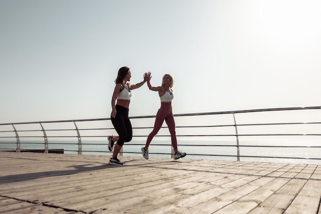 High five Two athletic women friends jogging along the embankment in the early morning Healthy lifestyle