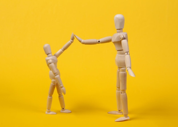 High five. Two wooden puppets on a yellow background