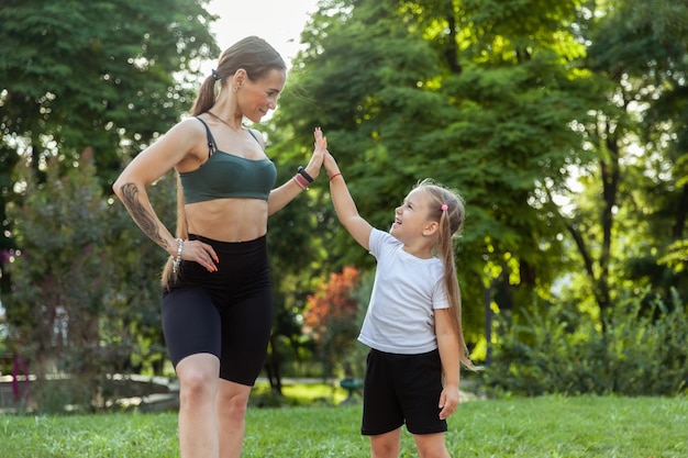 High five Young athletic mom with little daughter in the park