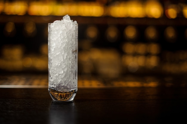 High glass with ice cubes on the bar counter of restaurant against the blurred background of lights