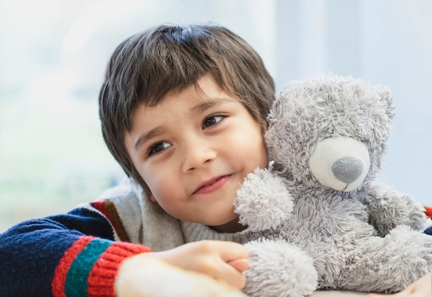 High key light portret schattige jongen zijn hoofd op teddybeer leggen en uitkijken met mooie bruine ogen