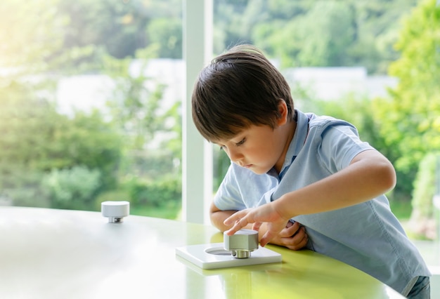 Alto ritratto chiave del bambino della scuola che gioca nella stanza dei giochi, bambino che tiene il gioco in basso con la faccia meravigliata in una stanza soleggiata accanto alla finestra, impara e gioca, concetto di educazione