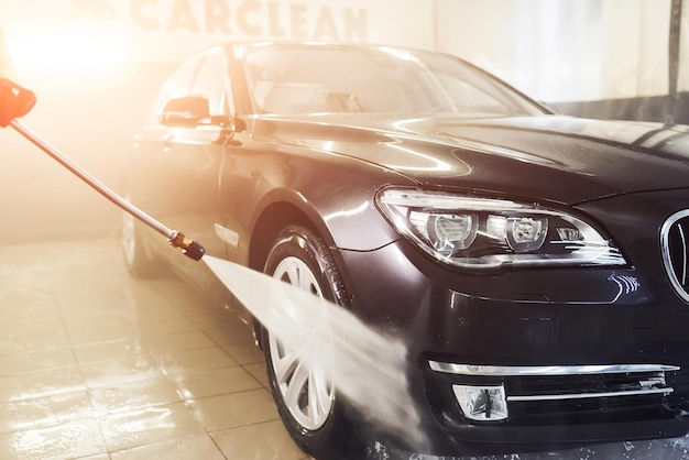 High pressured water Modern black automobile get cleaned inside of car wash station