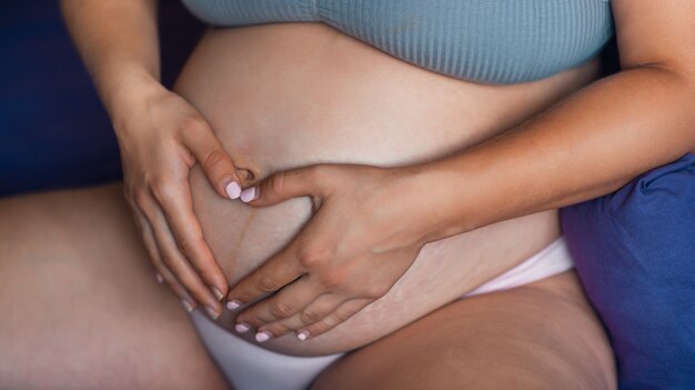 High resolution photo pregnancy. Pregnant woman's stomach is close-up. Heart with hands on the stomach. A woman strokes her stomach. Natural skin texture. Damaged skin with stretches, scars, stripes