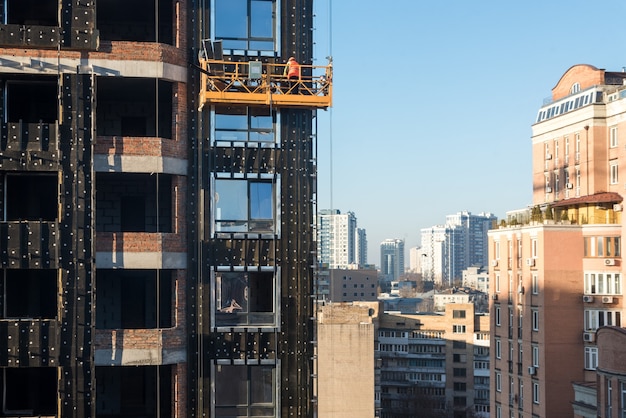 Foto lavori di costruzione di grattacieli, operai di cantiere nelle culle che lavorano con la facciata, culla sospesa per i costruttori che lavorano fuori dal grattacielo, costruzione di edifici.