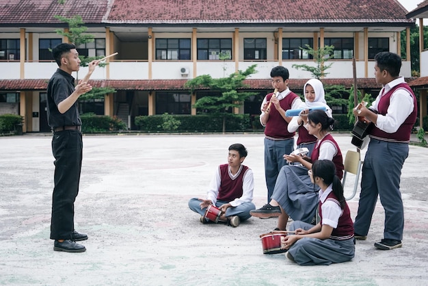 high school asian teacher leading students playing music instruments at school field