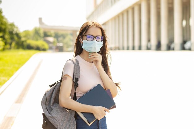 High school covid protection Vaccinated students back to college after covid19 pandemic over teenager girl with a backpack and books is standing next to the university medical plaster on hand