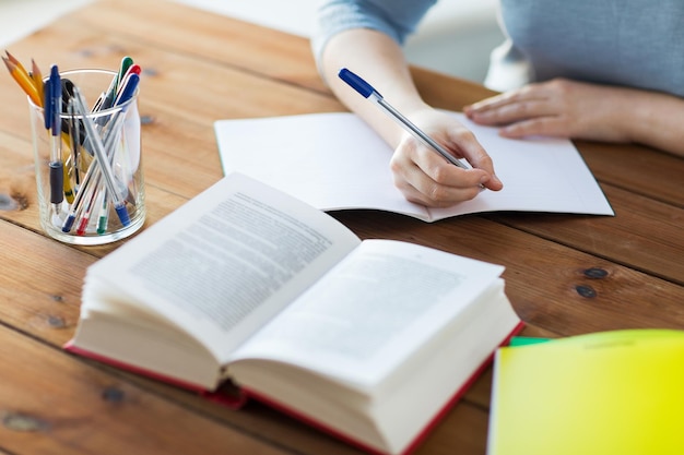 high school, education, people and learning concept - close up of young student or woman with book writing to notebook at home