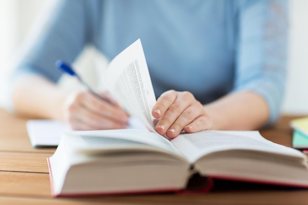 high school, education, people and learning concept - close up of young student or woman with book writing to notebook at home