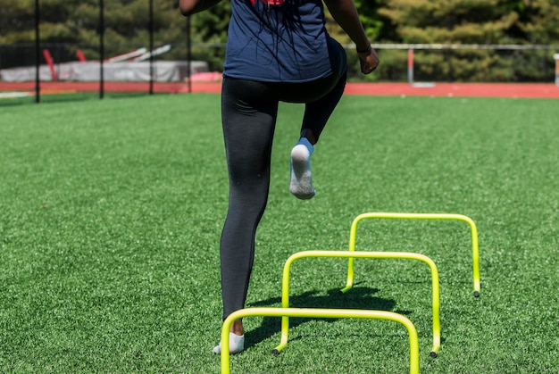 A high school girl is performing speed and agility drills over hurdles with no shoes on