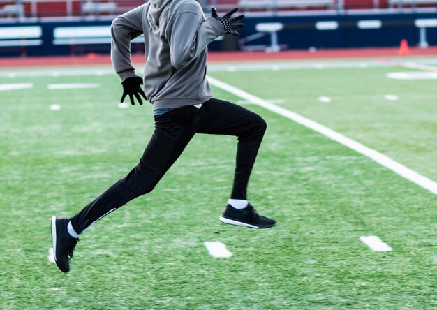 A high school sprinter is running fast on a green turf field during winter track and field practice