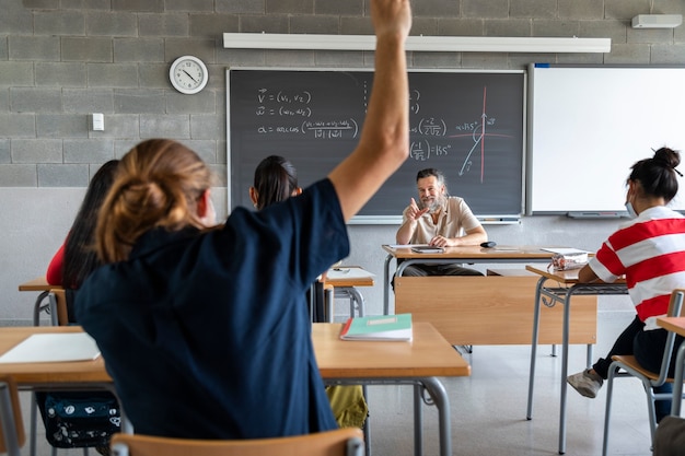 High school student raises hand to ask question Mature white man teacher grants permission to talk