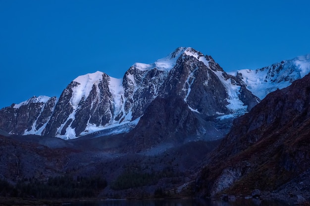 High snowy mountains illuminated by the light of the moon in a clear sky at dusk