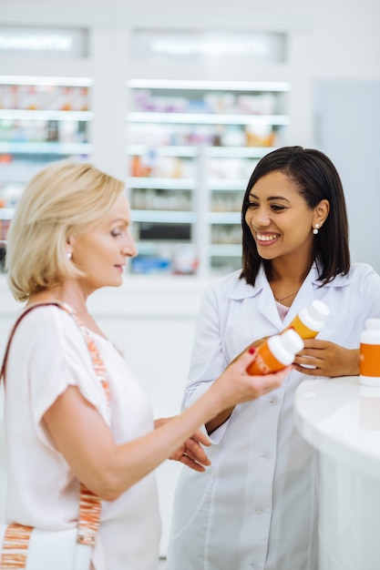 High spirited. Attentive blonde woman standing in semi position and looking at bottle with vitamins