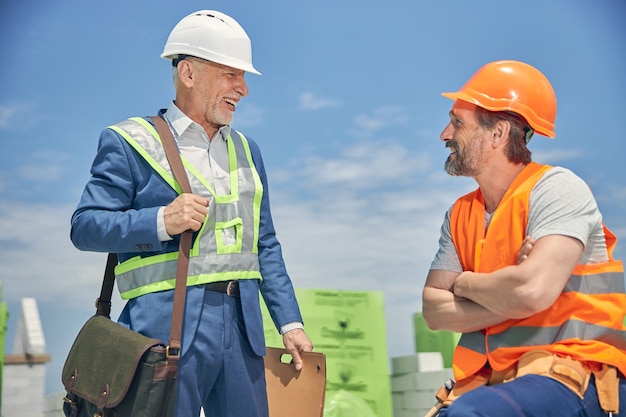 High-spirited stylish civil engineer with a bag over his shoulder looking at a pleased builder