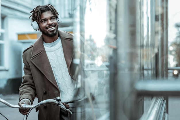 High spirits. Pleased international man keeping smile on his face while listening to music