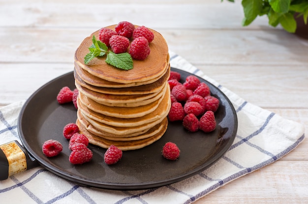 A high stack of vanilla pancakes in a pan with raspberry berries on top