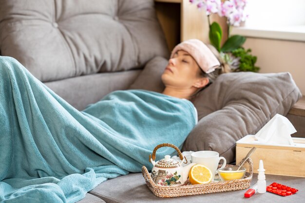 Photo high temperature a sick woman sleeps under a blanket on the sofa with a small towel on forehead