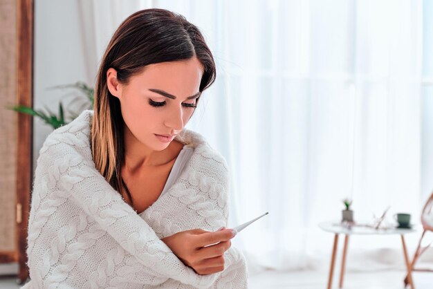 High temperature Sick young women looking thermometer while sitting on the sofa at home Copy space