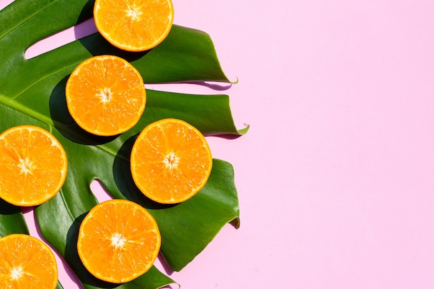 High vitamin C, Juicy and sweet. Fresh orange fruit with monstera plant leaf on pink background.