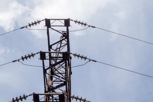 高電圧電気タワー。青い空に円形の雲がある晴れた日の送電線と送電鉄塔。高圧送電線がサポートします。それらは複雑な鉄骨構造を持っています。