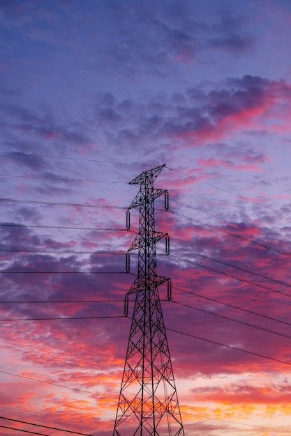 Столб пилона электричества высокого напряжения с небом и облаком красочным фоном заката